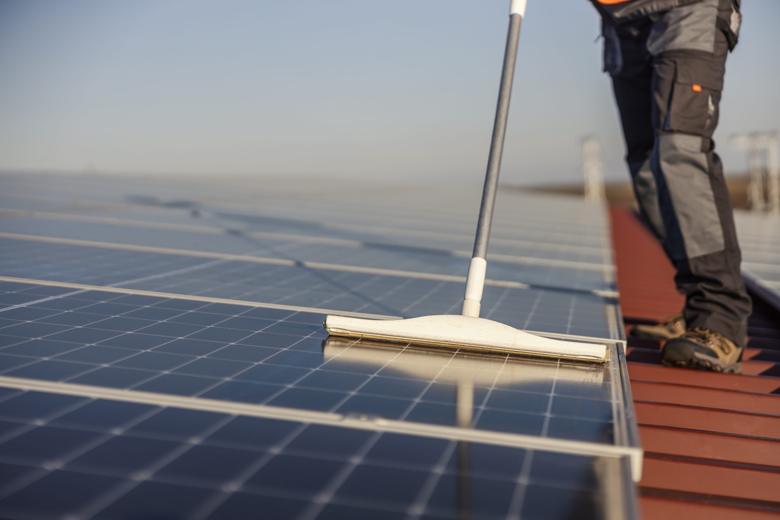 Services 18 Close up picture of a laborer cleaning solar panels with broom.