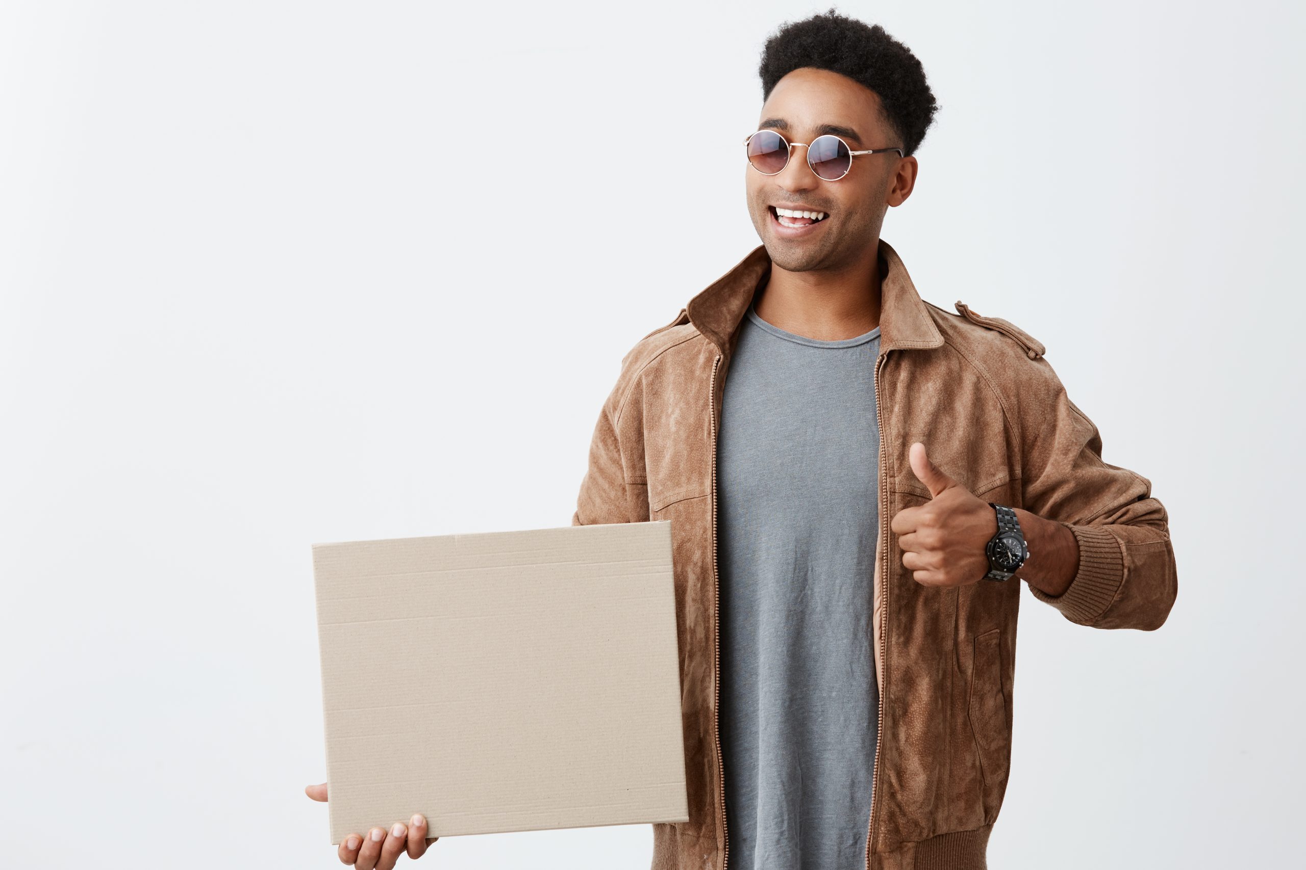 Services 23 Isolated portrait of young dark-skinned african male student with curly hair in casual trendy outfit and sunglasses holding paper board, showing thumb up, smiles brightly. Positive emotions.