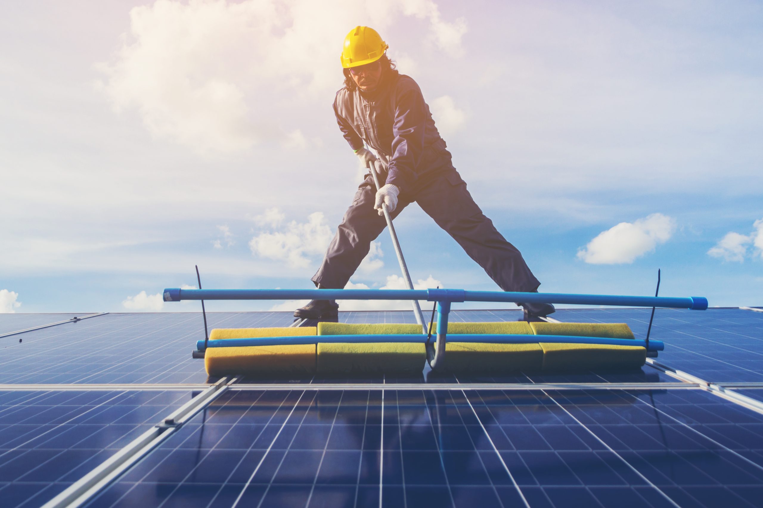 Services 21 technician operating and cleaning solar panels at generating power of solar power plant; technician in industry uniform on level of job description at industrial